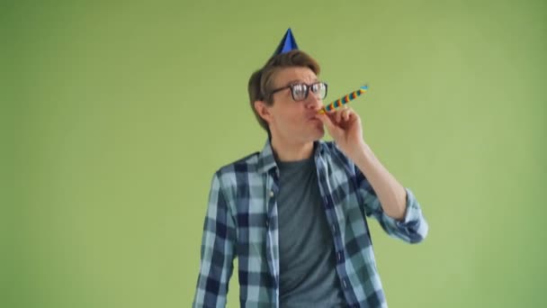 Portrait of happy birthday man in bright hat blowing party horn and laughing — Stock Video