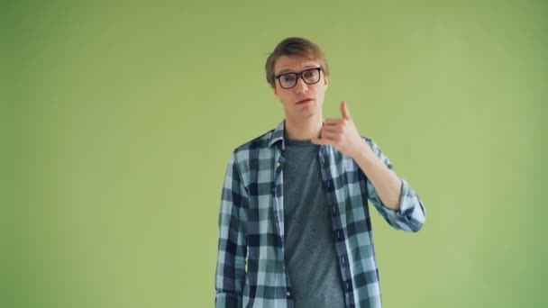 Porträtt av leende man som visar Call Me-gest stående på grön bakgrund — Stockvideo