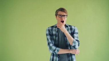 Sıkılmış genç adamın kameraya bakarak esneme portresi sonra kollarını geçiş