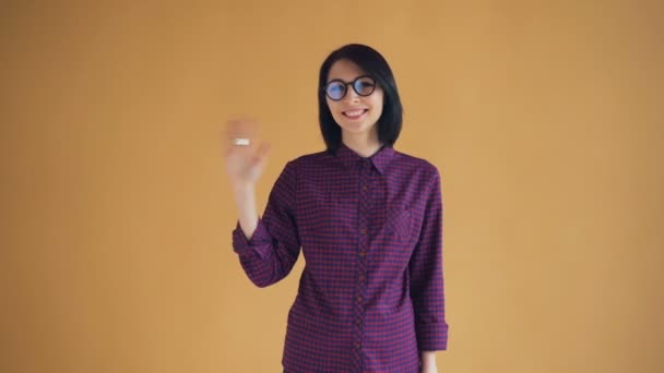 Retrato de linda mujer joven en gafas saludando con la mano y l saludo sonriente — Vídeos de Stock