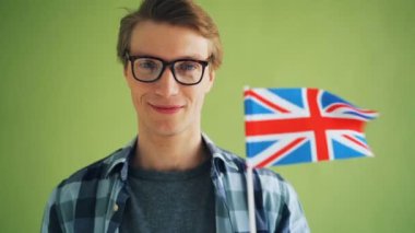 Rüzgarda el sallayarak İngiliz bayrağı tutan gülümseyen adamın yakın çekim yavaş hareket