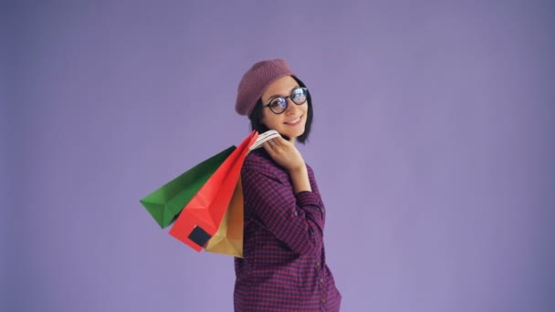 Retrato de jovem senhora feliz em óculos e chapéu elegante segurando sacos de compras — Vídeo de Stock