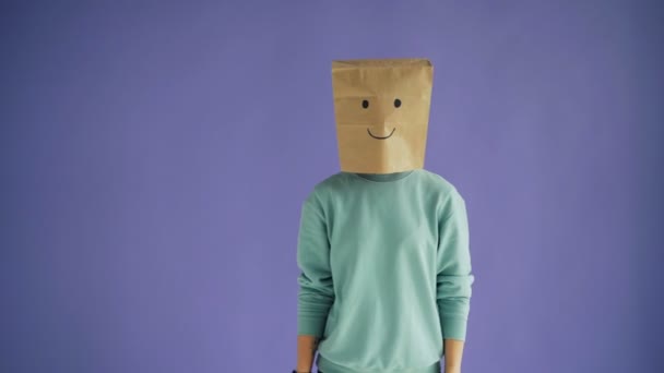 Retrato de mujer joven con bolsa de papel en la cabeza moviéndose a la cámara con la cara sonriente — Vídeos de Stock