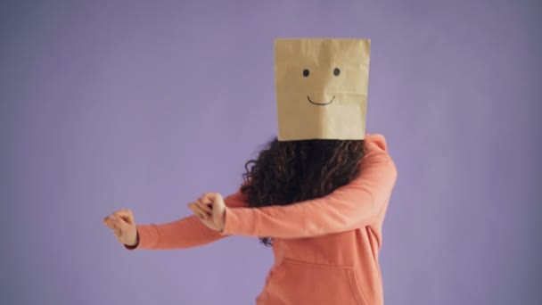 Jente med papirpose på hodet danser med tommeltotter opp og viser seg som et tegn – stockvideo