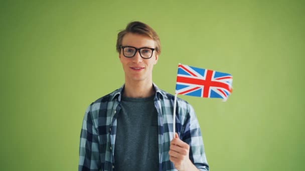 Retrato en cámara lenta del joven guapo sosteniendo la bandera oficial británica sonriendo — Vídeos de Stock