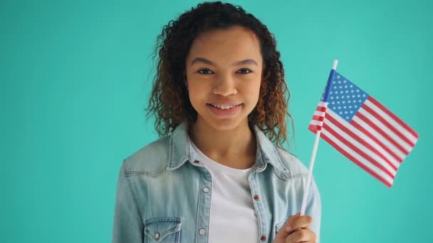 Повільний рух змішана гонка дівчина тримає американський прапор посміхаючись на синьому фоні — стокове відео