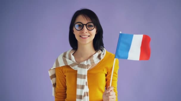 Cámara lenta de linda joven morena en gafas sosteniendo la bandera francesa sonriendo — Vídeo de stock