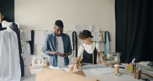 Aparadores creativos diseñando ropa usando tableta y cinta métrica en el estudio — Vídeos de Stock