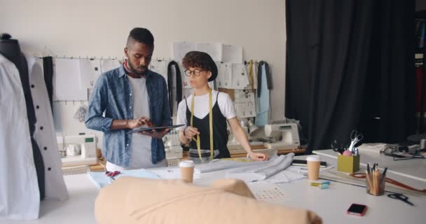 Diseñadores de moda de chica y chico que miden textiles y usan tabletas en estudio — Vídeo de stock