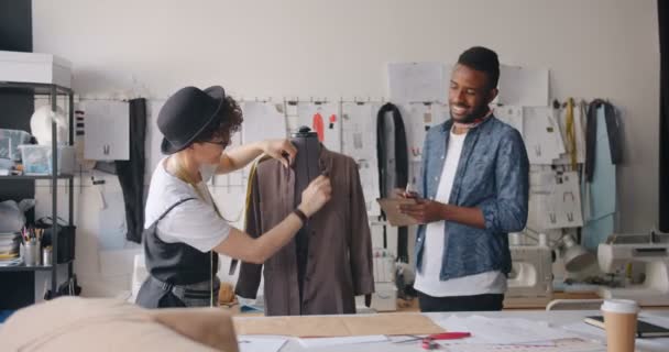 Des créateurs de vêtements souriants mesurant avec du ruban à mesurer prennent des notes dans un carnet — Video