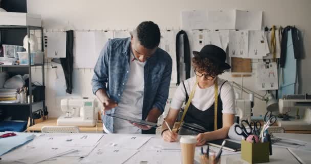 Чоловік і жінка дизайнери одягу використовують ескізи на планшеті в студії — стокове відео