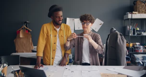 Paar ontwerpers schieten platte lay nemen foto van schetsen op naaien tabel — Stockvideo