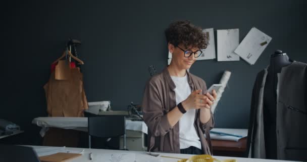 Moderne naaister met smartphone op het werk aanraken scherm texting glimlachend — Stockvideo