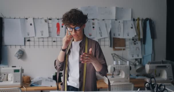 Ambicioso diseñador de moda hablando en el teléfono móvil en el taller de celebración de papeles — Vídeo de stock