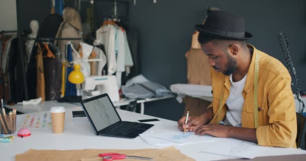 Σχεδιαστής ρούχων που σχεδιάζει κοιτάζοντας την οθόνη του φορητού υπολογιστή εργάζονται μόνοι στο στούντιο — Αρχείο Βίντεο