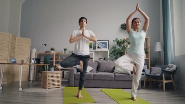 Sportigt par gör yoga övningar hemma balansering på ett ben stående på mattor — Stockvideo