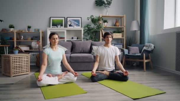 Jongeman en dame ontspannen in lotuspositie mediterend op de vloer thuis — Stockvideo