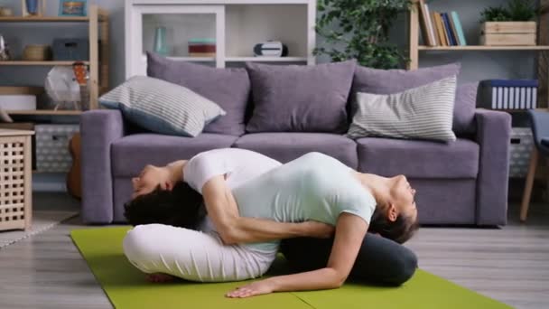 Гнучкий чоловік і дружина вправляються вдома разом роблячи йогу для пар — стокове відео