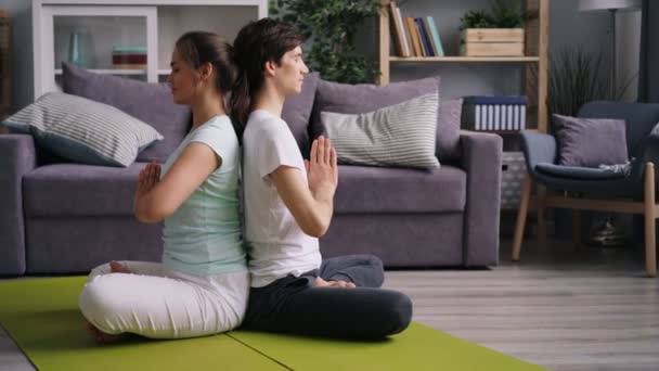 Namaste elleri ile arka arkaya oturan meditasyon genç çift yan görünümü — Stok video