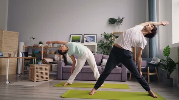 Hombre y mujer en familia de ropa deportiva haciendo yoga en apartamento moderno — Vídeos de Stock