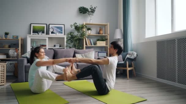 Glada par gör yoga hemma balansering i sittande ställning hålla händerna — Stockvideo