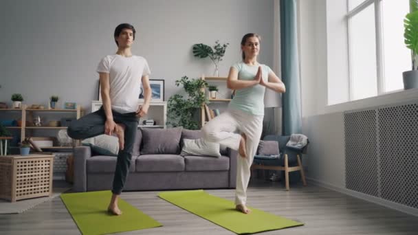 Молодая семья практикует йогу в квартире балансируя на одной ноге на циновках — стоковое видео