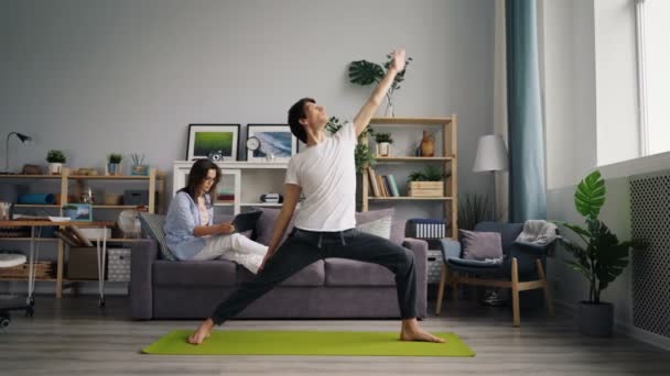 Mezcla de raza joven de ejercicio en casa haciendo yoga cuando la esposa charlando por teléfono — Vídeos de Stock