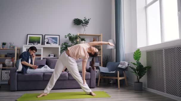 Kvinnlig student gör yoga medan man arbetar med laptop pratar på telefon — Stockvideo