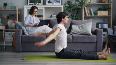 Kocası yoga yaparken karısı dizüstü bilgisayar kullanarak sosyal medya kontrol
