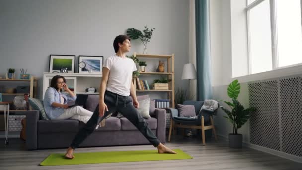 Spor koca dizüstü bilgisayar tutarak cep telefonu konuşurken kız yoga yaparken — Stok video