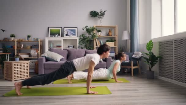 Chica y chico haciendo asanas de yoga en bonito apartamento de entrenamiento en esteras juntos — Vídeos de Stock