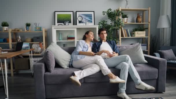 Zoom de adorable pareja viendo la televisión riendo comiendo palomitas de maíz juntos — Vídeos de Stock