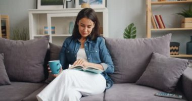 Genç kadın okuma kitap zevk edebiyat tutmak fincan çay içinde ev