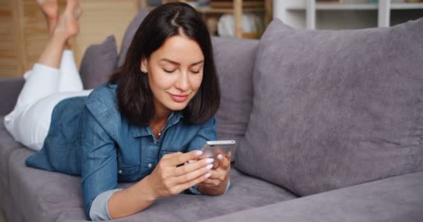 Sorrindo jovem usando smartphone segurando gadget tocando tela em casa — Vídeo de Stock