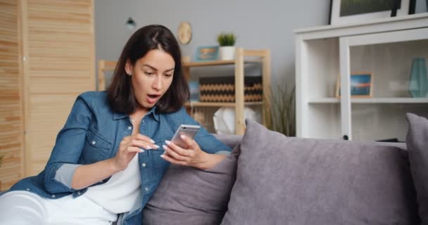 Jovem excitada celebrando o sucesso olhando para a tela do smartphone em casa — Vídeo de Stock