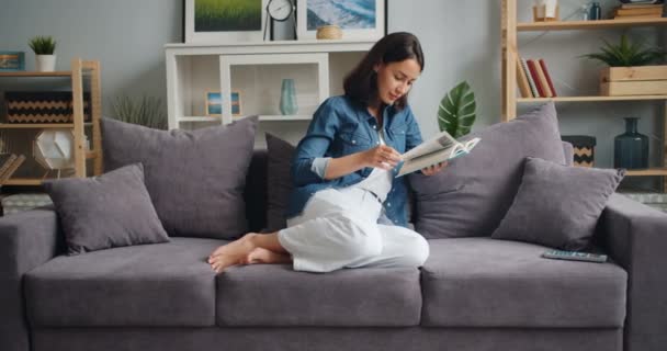 Cámara lenta de hermosa chica leyendo libro relajante en casa en bonito apartamento — Vídeo de stock