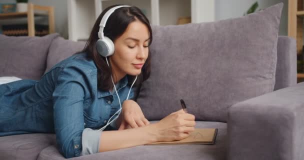 Creatief meisje luisteren naar muziek via een koptelefoon en tekening foto thuis — Stockvideo