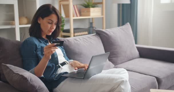 Menina bonita fazendo pagamento on-line segurando cartão usando laptop moderno em casa — Vídeo de Stock