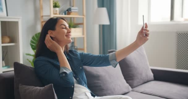 Ganska ung dam poserar för smartphone kamera tar selfie i lägenheten — Stockvideo