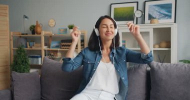 Neşeli kadın müzik hareketli el ve baş kanepede oturan evde dinleme