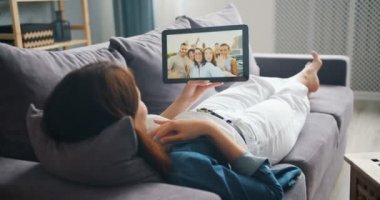 Genç kadın yapma video çağrı ile tablet konuşurken arkadaşlarıyla kanepede yatıyor