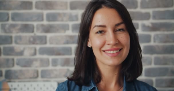 Close-up shot van de vrouw te kijken naar de camera glimlachen met bakstenen muur in de achtergrond — Stockvideo