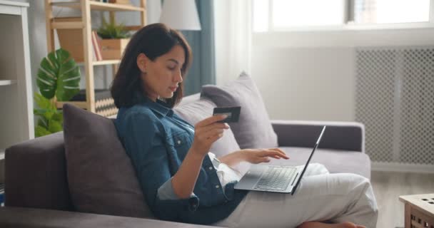 Movimento lento de compras menina on-line segurando cartão de crédito usando laptop em casa — Vídeo de Stock