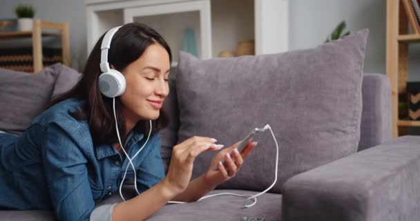 Happy student listening to music in headphones holding smartphone at home — Stock Video