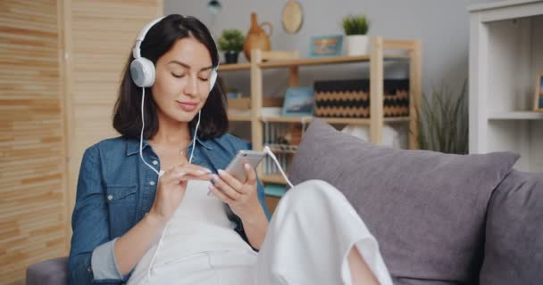 Hermosa mujer joven escuchando música a través de auriculares con teléfono inteligente — Vídeo de stock