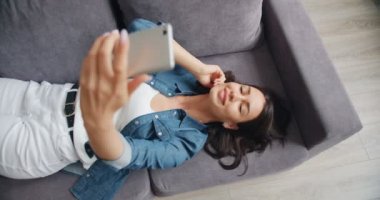 Akıllı telefon kamera kullanarak evde kanepede yatarken selfie çeken büyüleyici kız