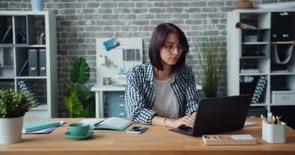 Портрет женщины, работающей с ноутбуком в офисе, а затем смотрящей в камеру улыбающейся — стоковое видео