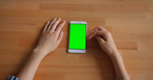 Γυναικεία χέρι αγγίζοντας πράσινο μακέτα οθόνη smartphone που βρίσκεται σε ξύλινο τραπέζι — Αρχείο Βίντεο