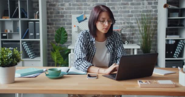 Офісний працівник використовує ноутбук, а потім пише в блокноті, сидячи за столом на робочому місці — стокове відео