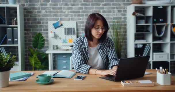 Porträt eines hübschen Mädchens, das bei der Arbeit auf dem Laptop tippt und dann lächelnd in die Kamera blickt — Stockvideo